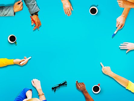 A circle of hands reaching into the middle of an empty table showing collaboration and participation. 
